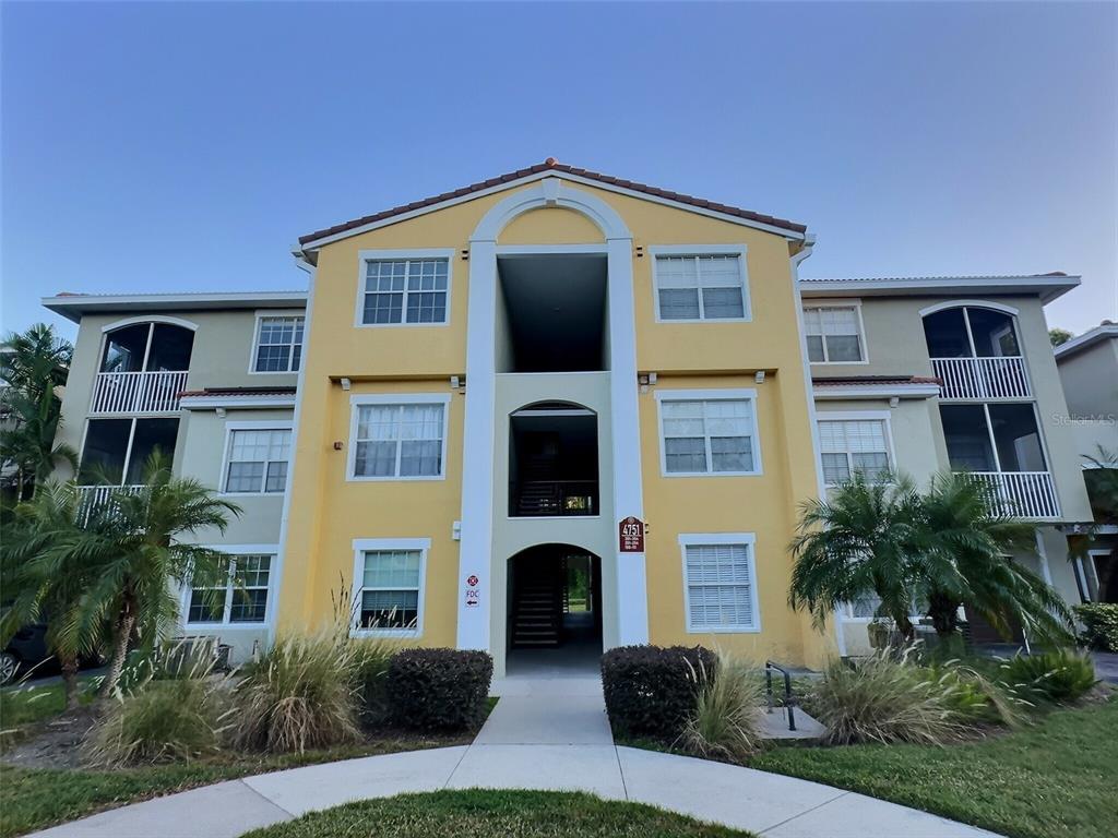 A three-story yellow apartment building with a central breezeway and screened balconies — 4751 TRAVINI CIRCLE UNIT 4-105, SARASOTA, FL