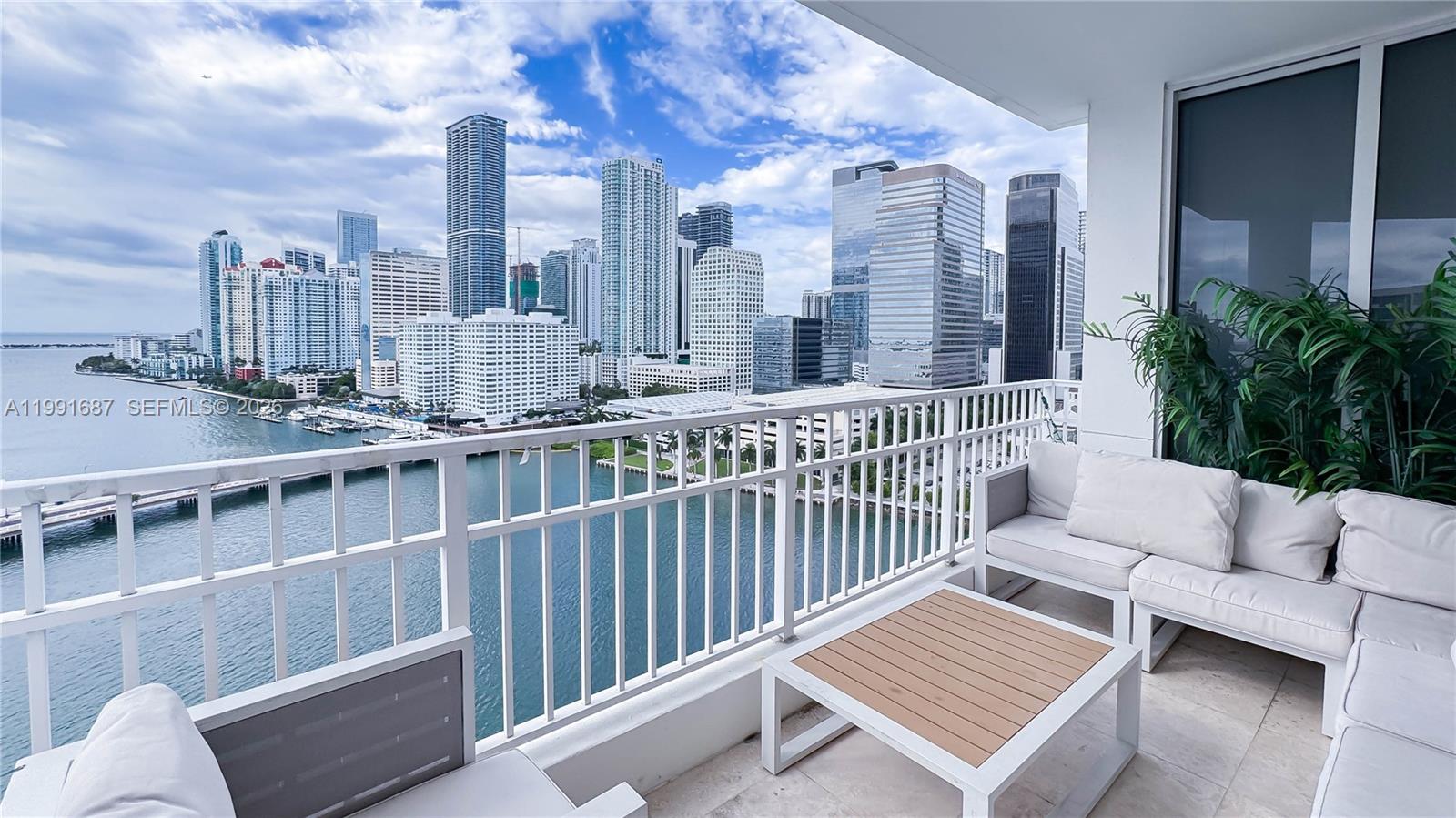 A balcony with white outdoor furniture overlooks a bay and the Miami city skyline — 701 Brickell Key Blvd # 1912, Miami FL 33131, MIAMI, FL