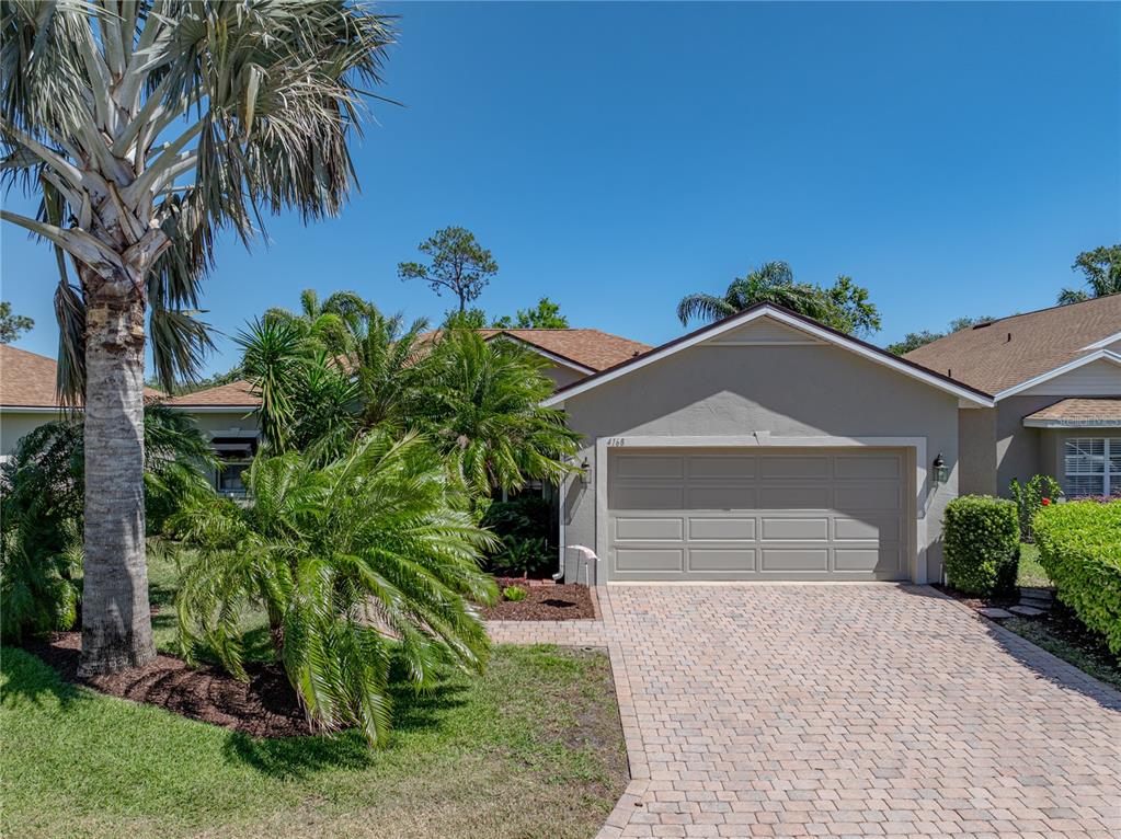 A single-story house with a beige garage, a brick paver driveway, and lush tropical landscaping — 4168 ABERDEEN LANE, LAKE WALES, FL