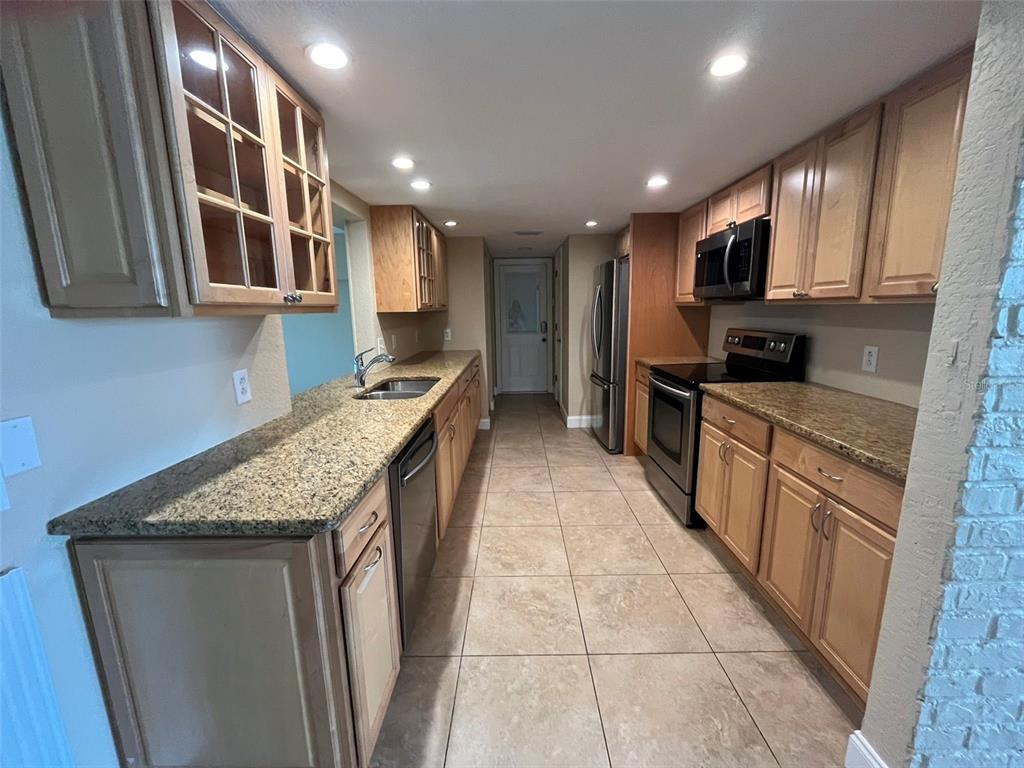 A galley kitchen features light wood cabinets, granite countertops, stainless steel appliances, and tile flooring — 671 SPRING LAKE BOULEVARD NW, PORT CHARLOTTE, FL