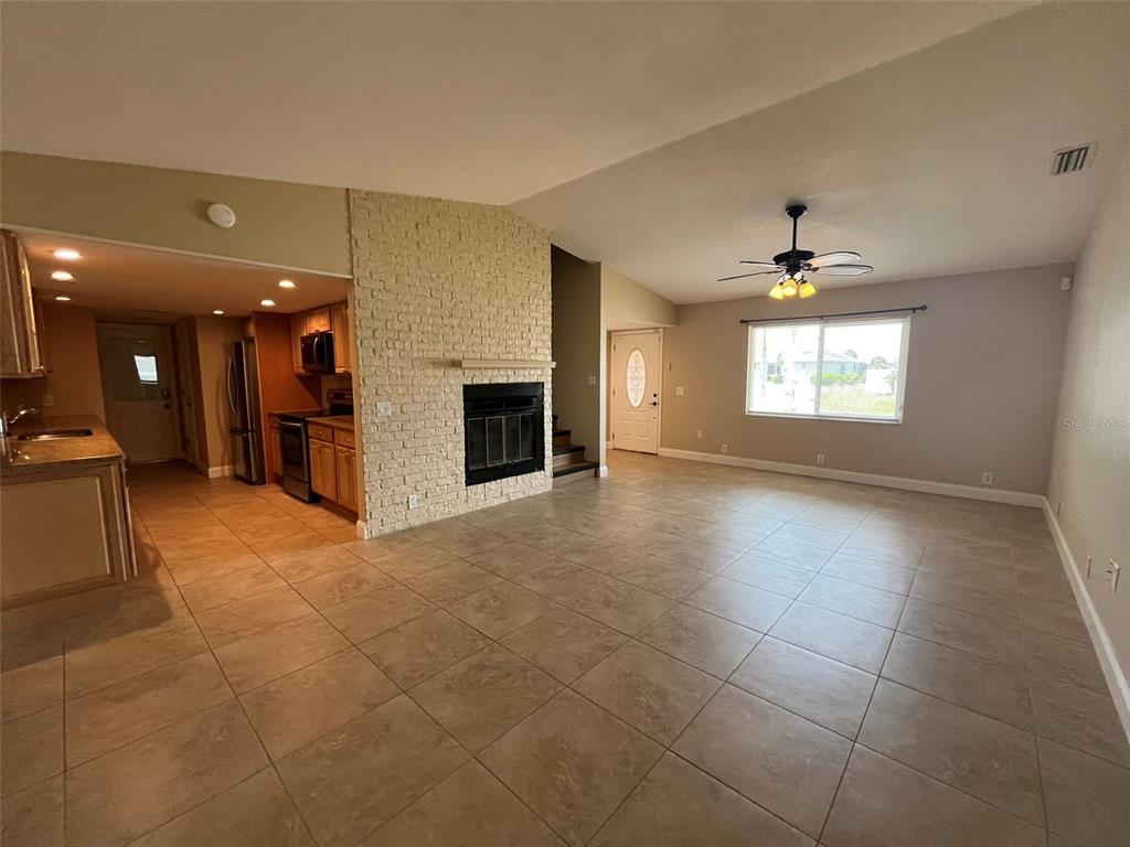 A living room with tile flooring, a brick fireplace, and an adjacent open kitchen — 671 SPRING LAKE BOULEVARD NW, PORT CHARLOTTE, FL