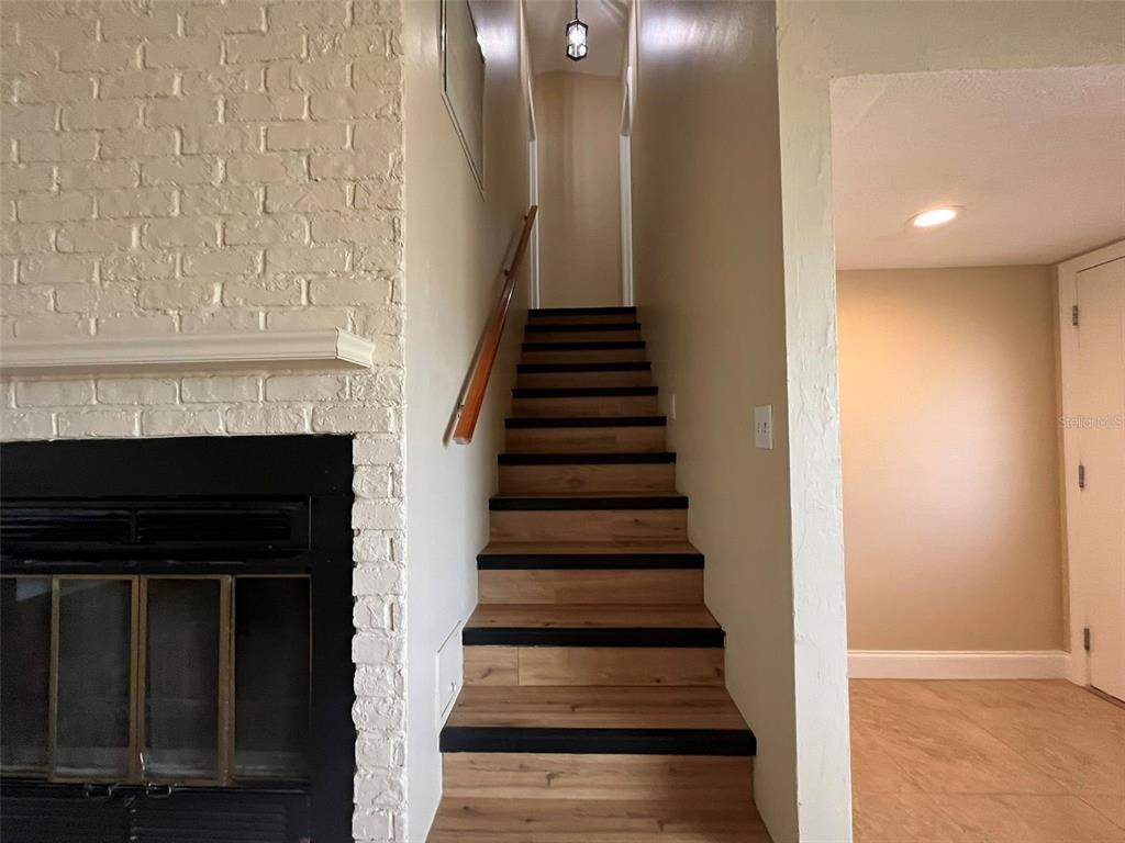 A staircase with wood treads and a handrail sits beside a white brick fireplace — 671 SPRING LAKE BOULEVARD NW, PORT CHARLOTTE, FL