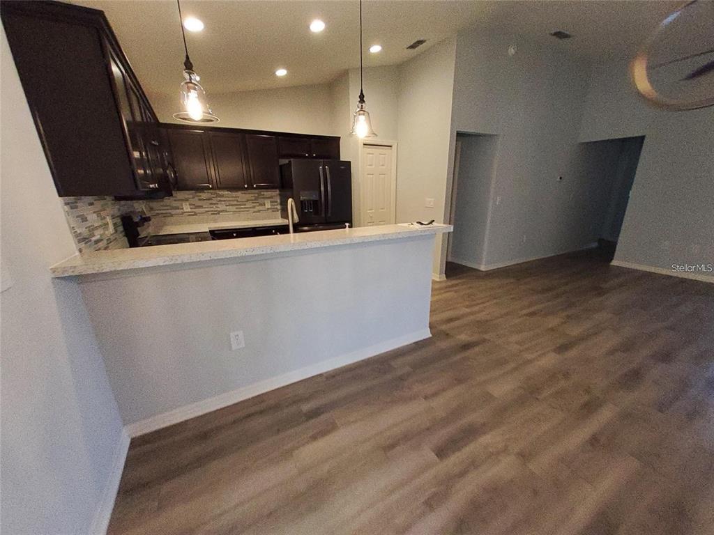A kitchen features dark cabinets, a light-colored countertop, and a breakfast bar overlooking a room — 1531 WOODLARK DRIVE, HAINES CITY, FL