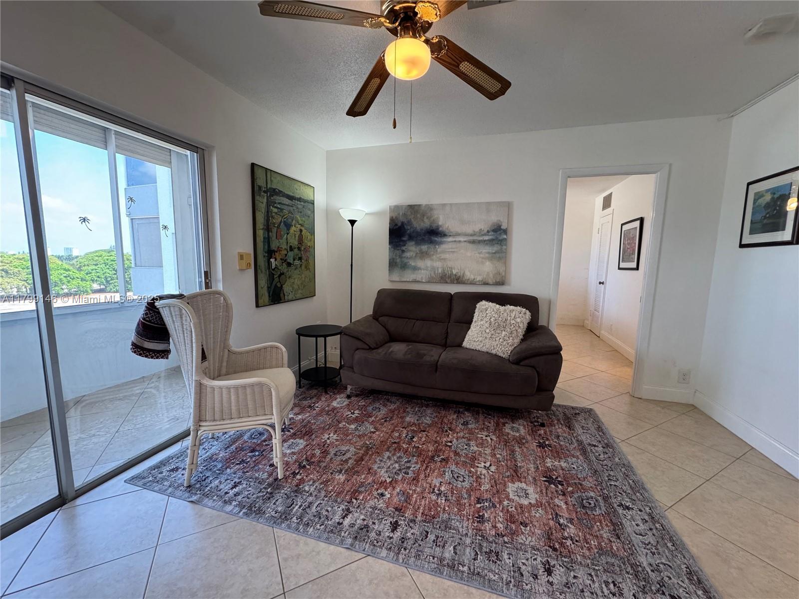 A living room features a brown sofa, a wicker chair, and a patterned area rug — 1700 Pierce St # 702, Hollywood FL 33020, HOLLYWOOD, FL