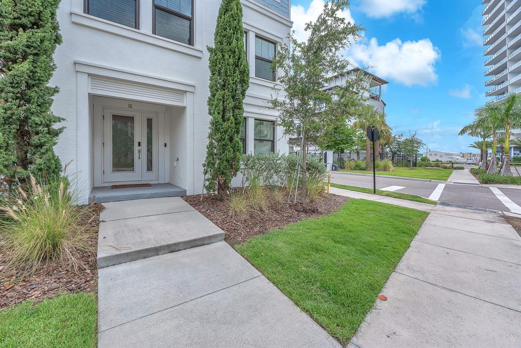 A white multi-story building entrance features a glass-paneled front door, landscaping, and a concrete walkway — 5351 BRIDGE STREET UNIT 16, TAMPA, FL