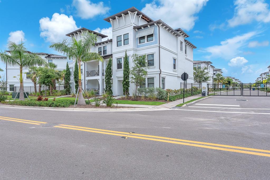 A multi-story white residential building stands behind a gated entrance next to a paved road — 5351 BRIDGE STREET UNIT 16, TAMPA, FL