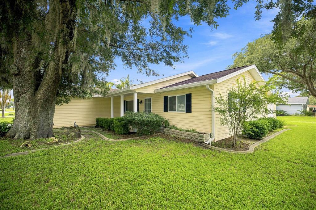 A yellow single-story house with a covered entryway and large oak tree in the yard — 10298 SE 176TH STREET, SUMMERFIELD, FL