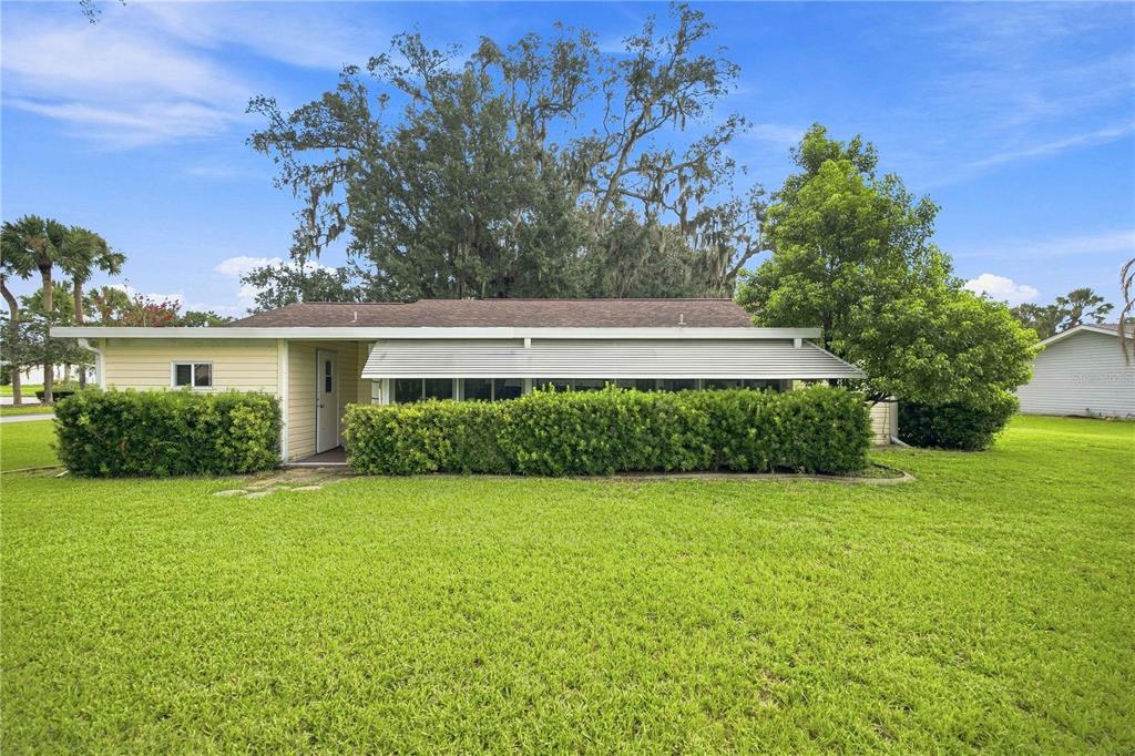 A single-story house with yellow siding, a metal awning, and a large hedge in front — 10298 SE 176TH STREET, SUMMERFIELD, FL