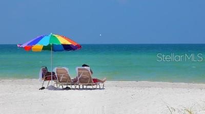 A person sits in a beach chair under a colorful umbrella on a sandy beach — 581 ROUNTREE DRIVE, LONGBOAT KEY, FL