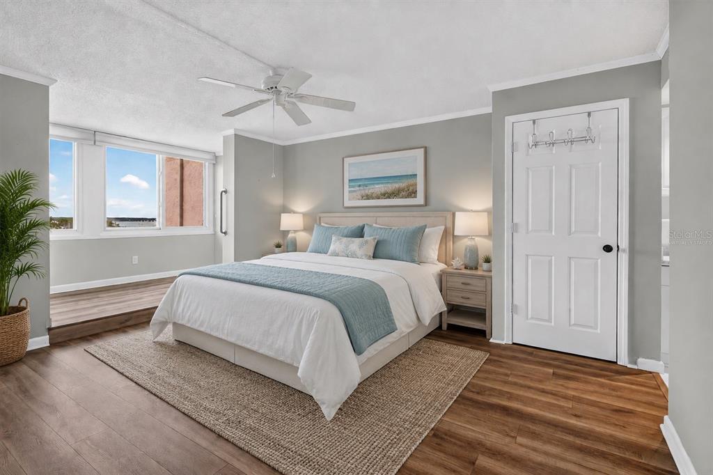 A bedroom with a queen bed, light gray walls, wood-look flooring, and a raised window area — 2621 COVE CAY DRIVE UNIT 802, CLEARWATER, FL