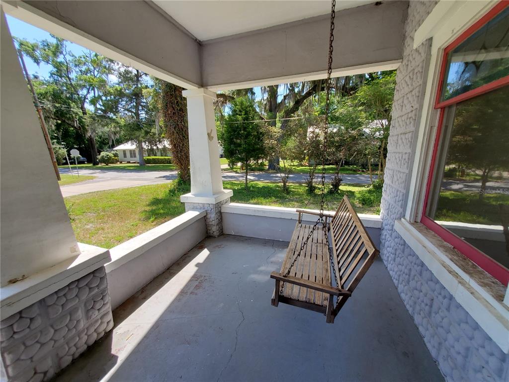 A covered front porch features a wooden swing, concrete flooring, and stone-accented support columns — 23882 NW 187TH AVENUE, HIGH SPRINGS, FL