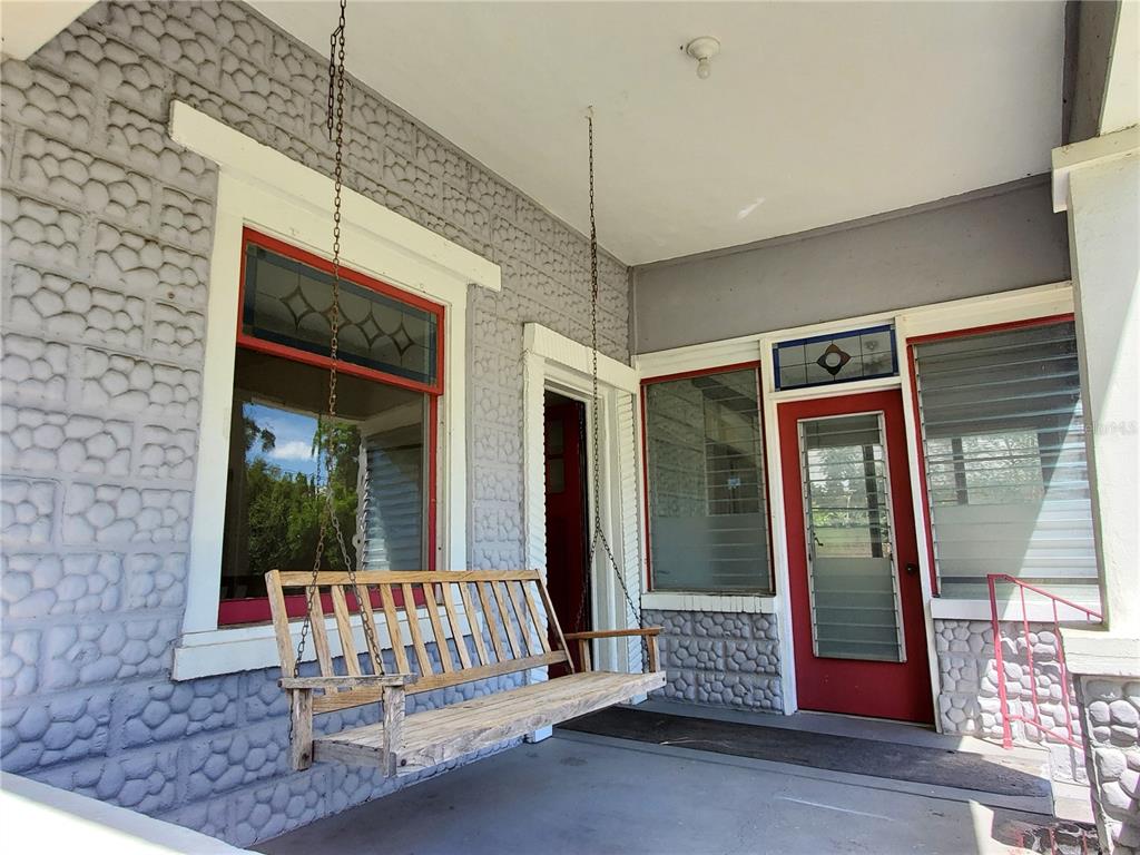 A covered porch features a hanging wooden bench, red-trimmed doors, and textured stone-patterned walls — 23882 NW 187TH AVENUE, HIGH SPRINGS, FL