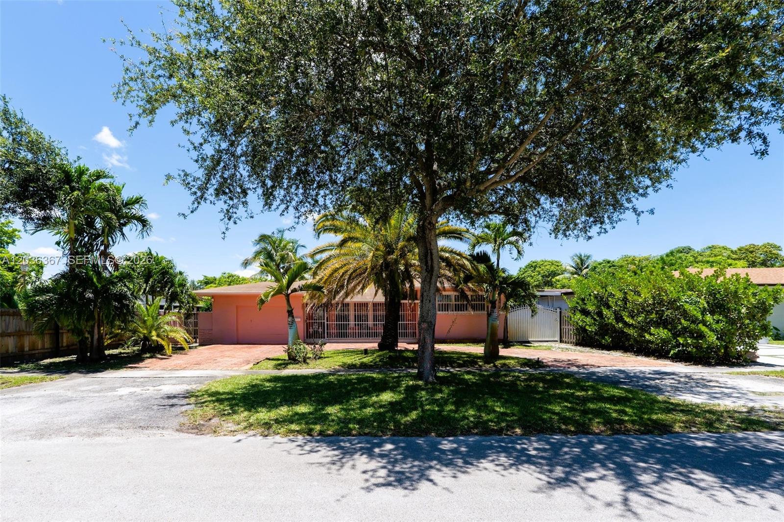 A pink single-story house features a brick driveway, palm trees, and a large shade tree — 315 NW 124th St, North Miami FL 33168, NORTH MIAMI, FL