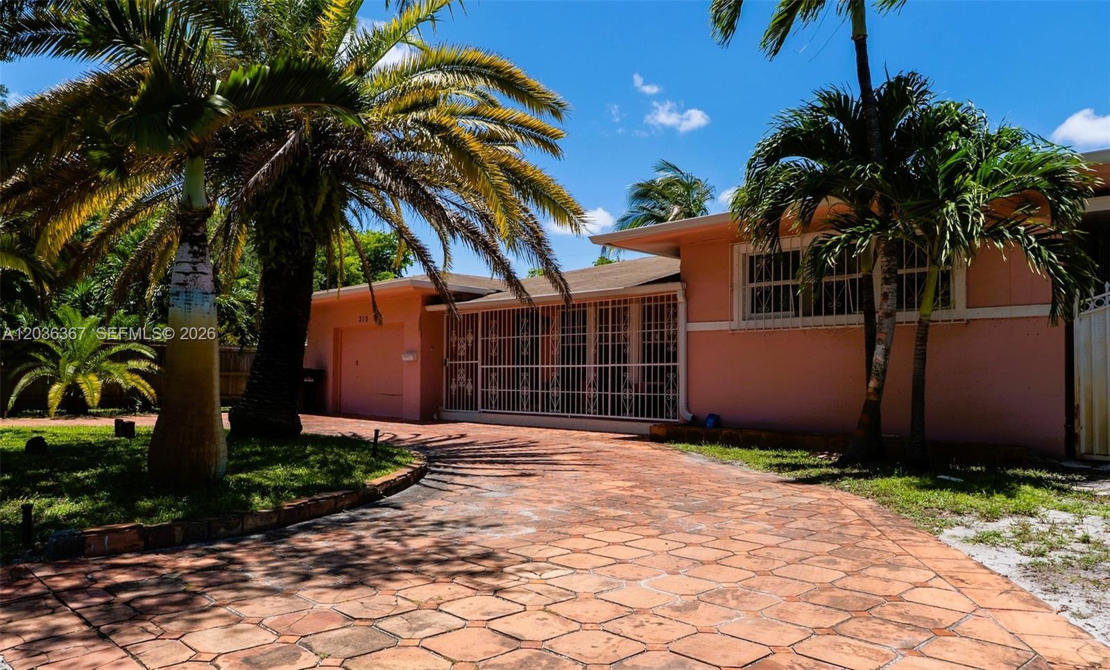 A single-story pink house features a stone driveway, palm trees, and white security bars — 315 NW 124th St, North Miami FL 33168, NORTH MIAMI, FL