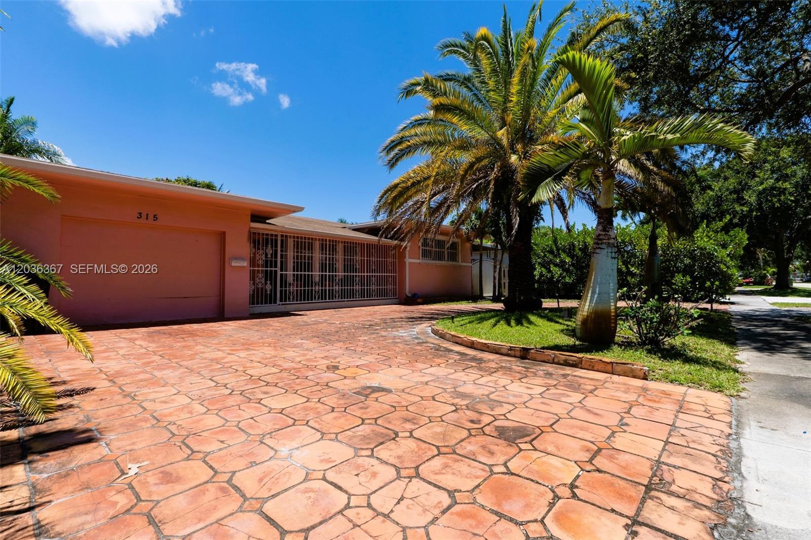 A single-story house with a pink exterior, a paved driveway, and a large palm tree — 315 NW 124th St, North Miami FL 33168, NORTH MIAMI, FL