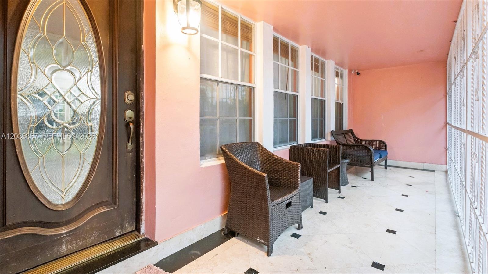 A covered porch features pink walls, tiled flooring, and three wicker chairs — 315 NW 124th St, North Miami FL 33168, NORTH MIAMI, FL