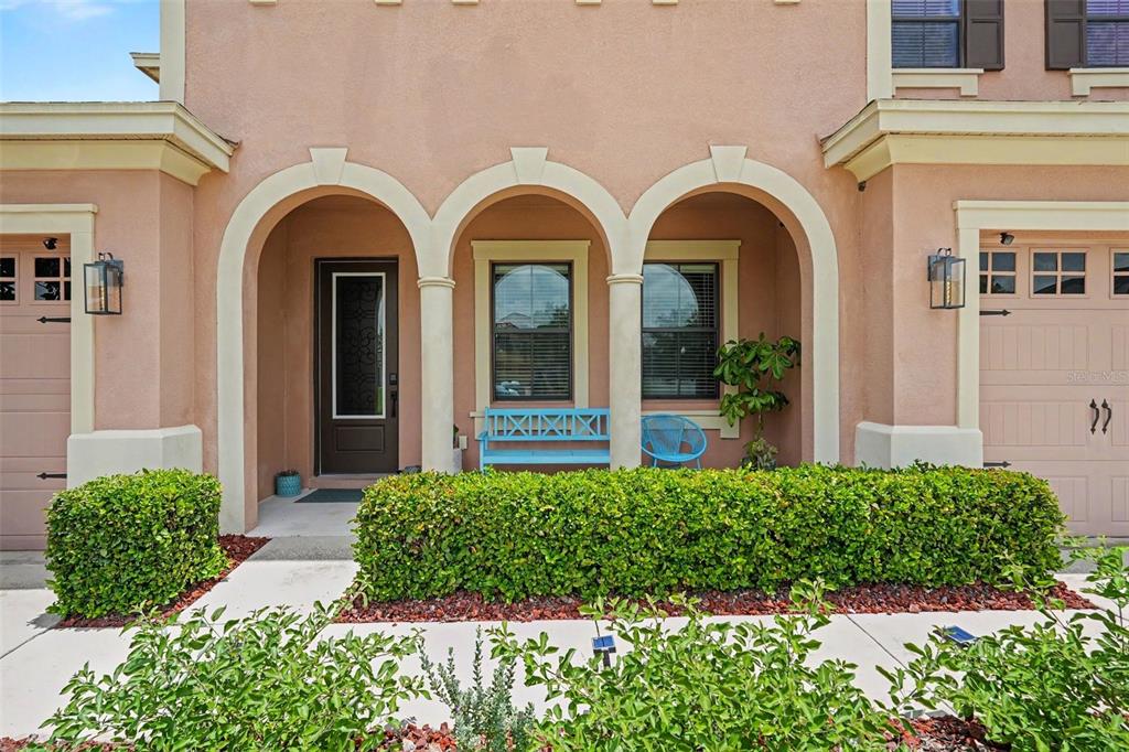 The exterior of a tan stucco home features three arched entryways, a front door, and landscaping — 7110 REDROOT COURT, WESLEY CHAPEL, FL