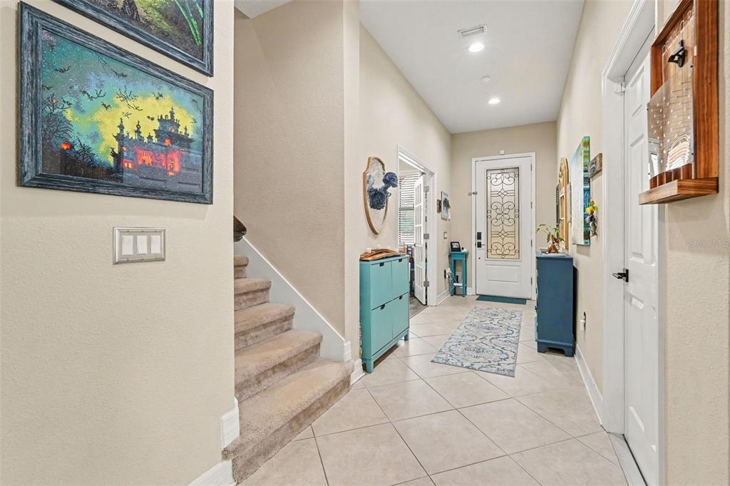 A tiled entryway features a staircase with carpeted steps, a front door, and blue furniture — 7110 REDROOT COURT, WESLEY CHAPEL, FL