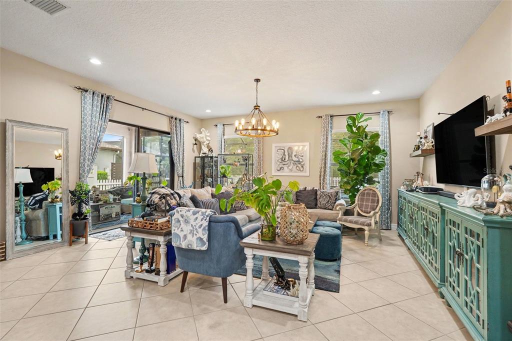A living room features tile floors, a blue sofa, a chandelier, and a large television — 7110 REDROOT COURT, WESLEY CHAPEL, FL