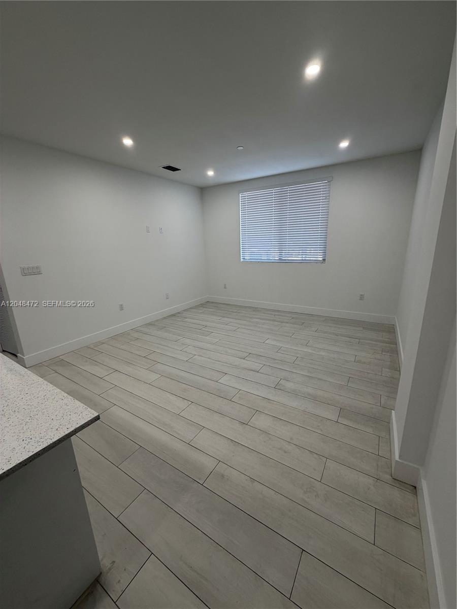 An empty room features white walls, recessed lighting, and light-colored wood-look tile flooring — 879 E 24th St # 203, Hialeah FL 33013, HIALEAH, FL