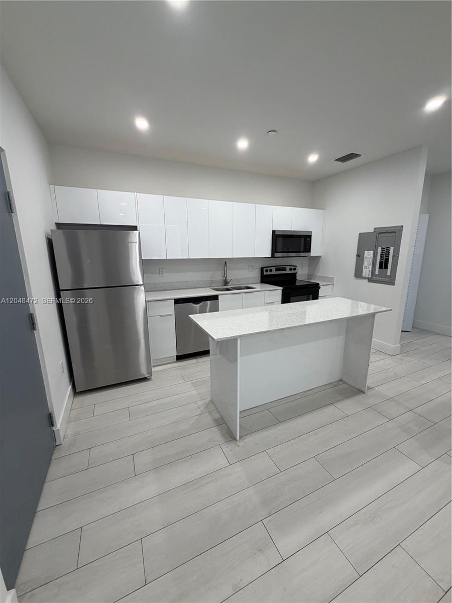 A modern kitchen features white cabinets, stainless steel appliances, a kitchen island, and light flooring — 879 E 24th St # 203, Hialeah FL 33013, HIALEAH, FL