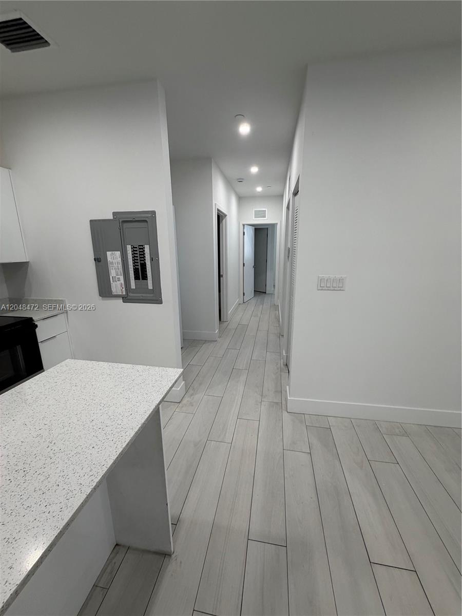 A hallway with light wood-look tile flooring leads past a kitchen area and electrical panel — 879 E 24th St # 203, Hialeah FL 33013, HIALEAH, FL