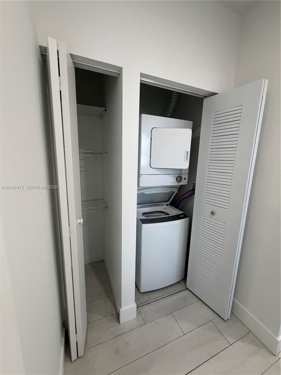 A laundry closet contains a stacked washer and dryer next to an empty storage shelf — 879 E 24th St # 203, Hialeah FL 33013, HIALEAH, FL