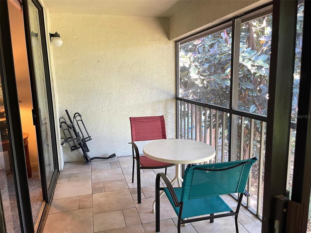 A screened-in balcony features tiled flooring, a small round table, and two outdoor chairs — 4601 46TH STREET COURT W UNIT 202B, BRADENTON, FL