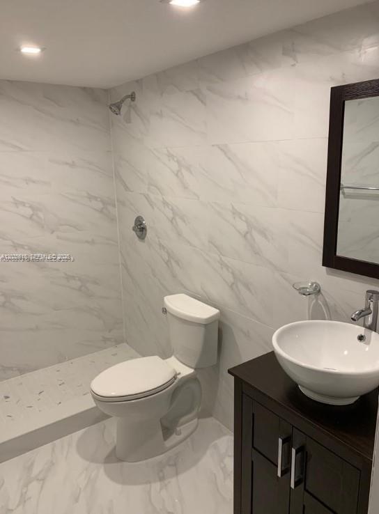 A bathroom features white marble-look tile walls, a white toilet, and a dark wood vanity — 6175 NW 186th St # 305, Hialeah FL 33015, HIALEAH, FL
