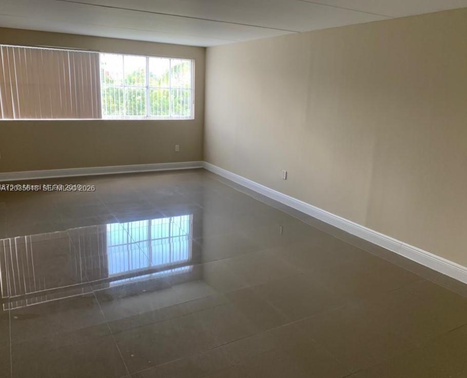 An empty room features beige walls, a large window, and glossy light-colored tile flooring — 6175 NW 186th St # 305, Hialeah FL 33015, HIALEAH, FL