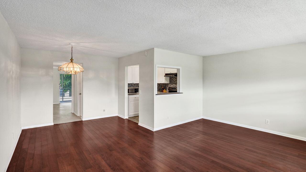 An empty living and dining area features dark wood flooring, light walls, and a kitchen pass-through — 118 Sheffield E, West Palm Beach FL 33417, WEST PALM BEACH, FL
