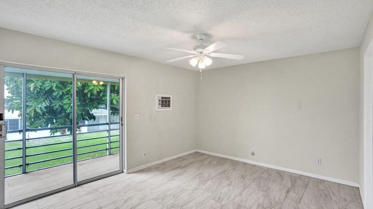 An empty room features light-colored wood-look tile flooring, a ceiling fan, and sliding glass doors — 118 Sheffield E, West Palm Beach FL 33417, WEST PALM BEACH, FL