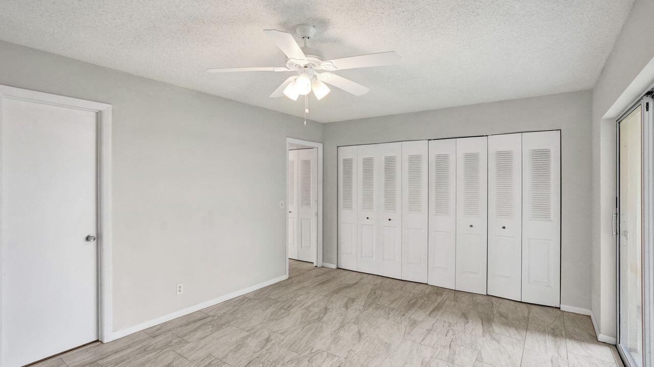 A bedroom with light gray walls, tile flooring, a ceiling fan, and white louvered closet doors — 118 Sheffield E, West Palm Beach FL 33417, WEST PALM BEACH, FL