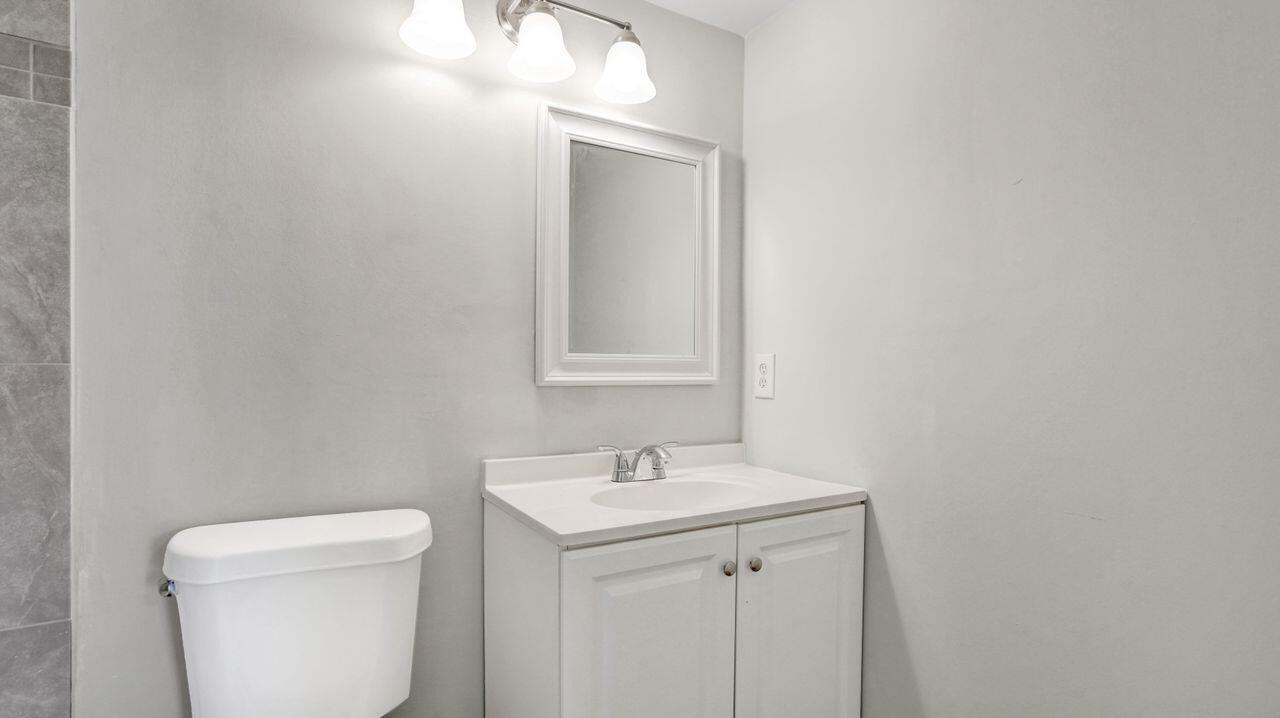 A bathroom features a white vanity with a sink, a mirror, and a toilet — 118 Sheffield E, West Palm Beach FL 33417, WEST PALM BEACH, FL