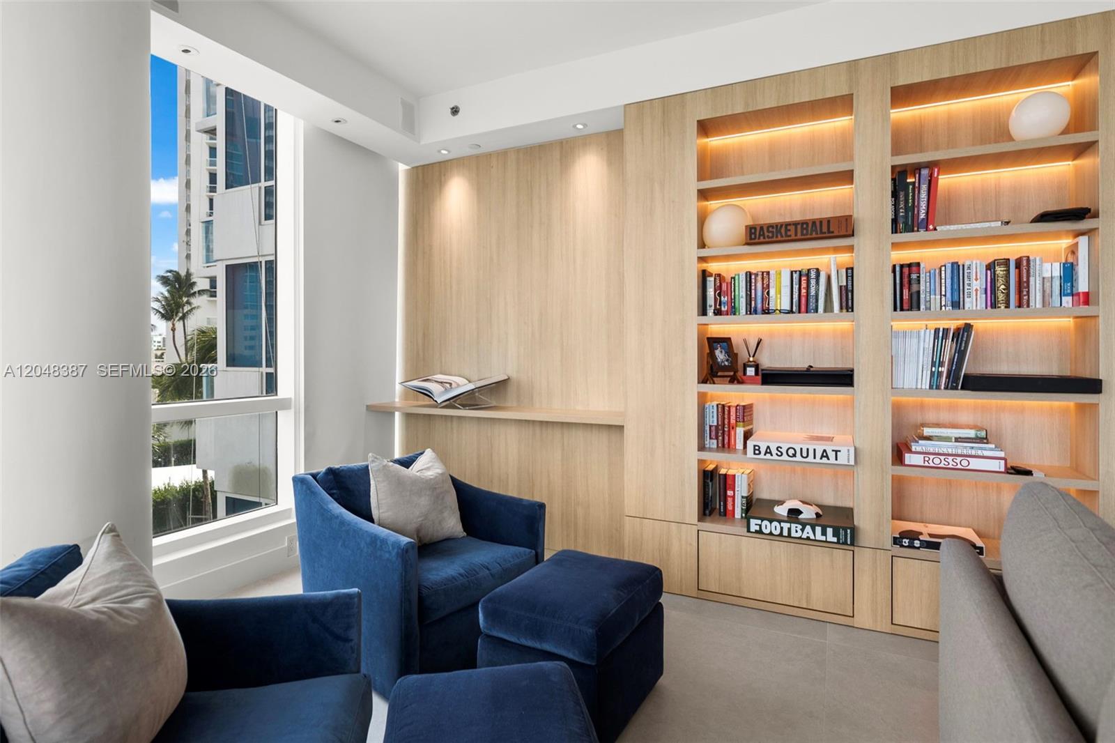 A modern room features built-in light wood shelving, blue armchairs, and a large floor-to-ceiling window — 100 S Pointe Dr # 501, Miami Beach FL 33139, MIAMI BEACH, FL