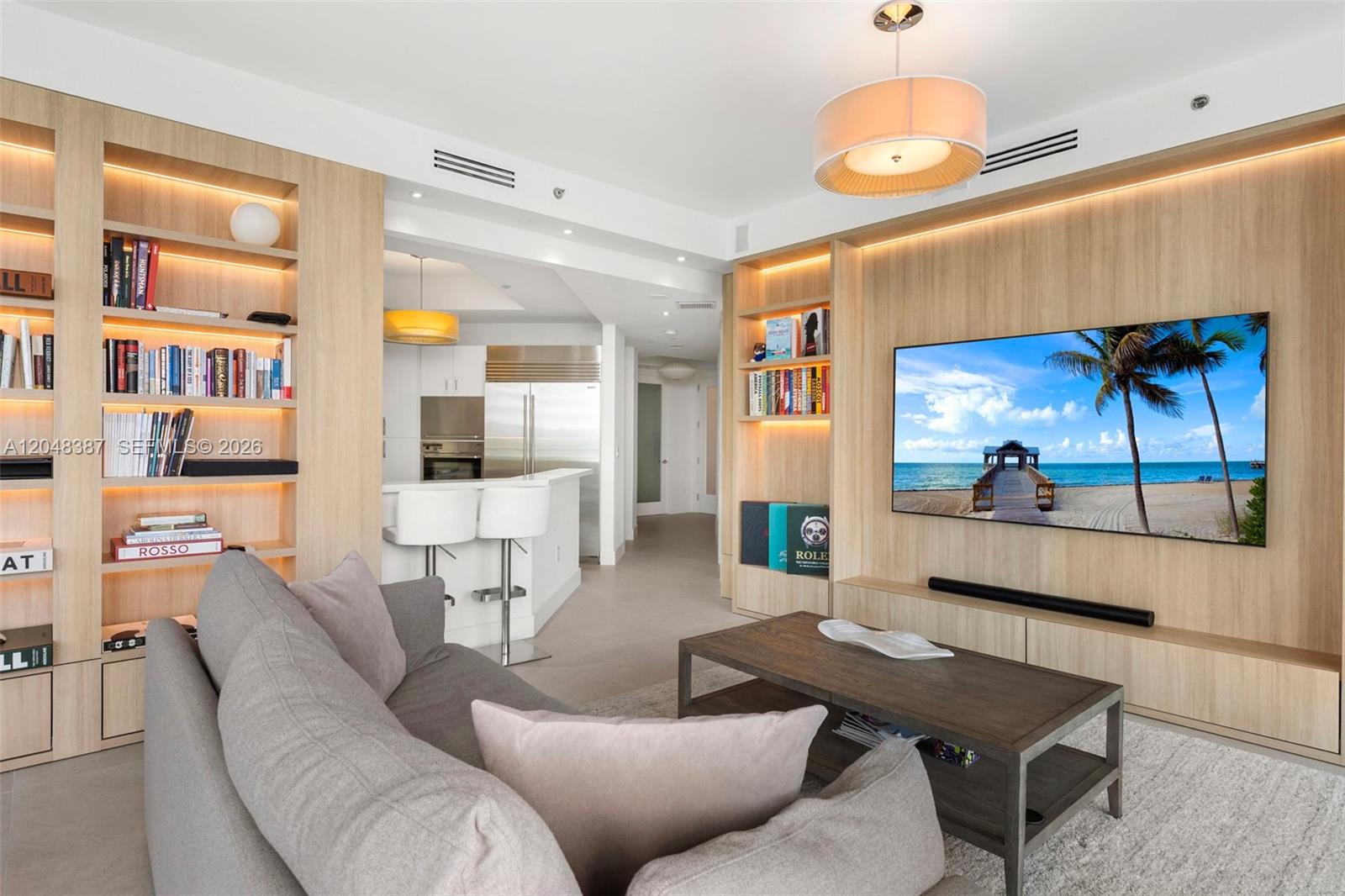A living room features light wood built-in shelving, a wall-mounted television, and a grey sofa — 100 S Pointe Dr # 501, Miami Beach FL 33139, MIAMI BEACH, FL