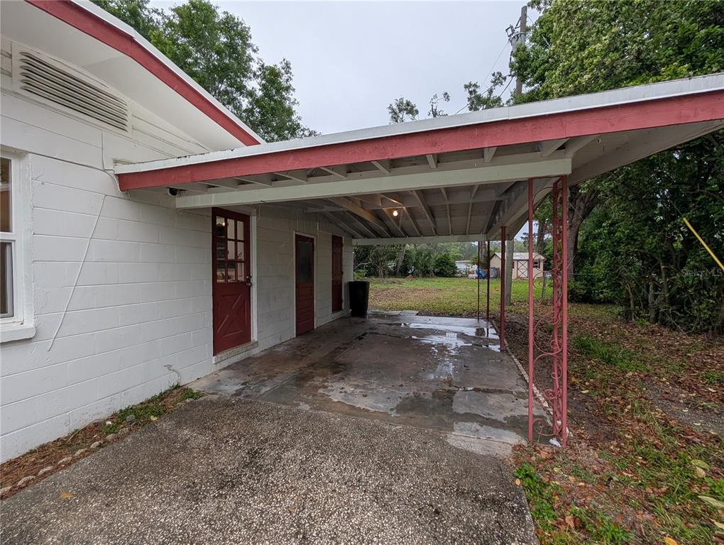 A concrete carport with a red-trimmed roof attached to a white block house — 208 OAKWOOD DRIVE, BROOKSVILLE, FL