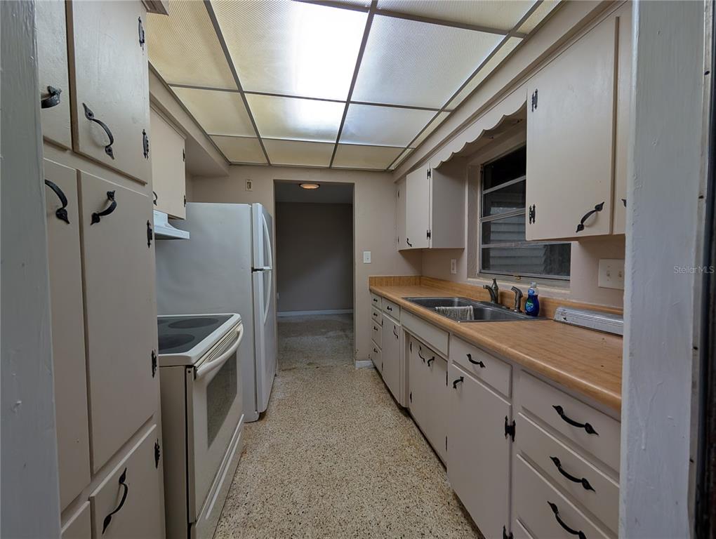 A galley kitchen features light-colored cabinets, wood-look laminate countertops, and a drop ceiling with lighting — 208 OAKWOOD DRIVE, BROOKSVILLE, FL