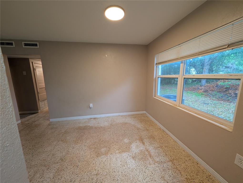 An empty room features beige walls, a large window with blinds, and stained carpet flooring — 208 OAKWOOD DRIVE, BROOKSVILLE, FL