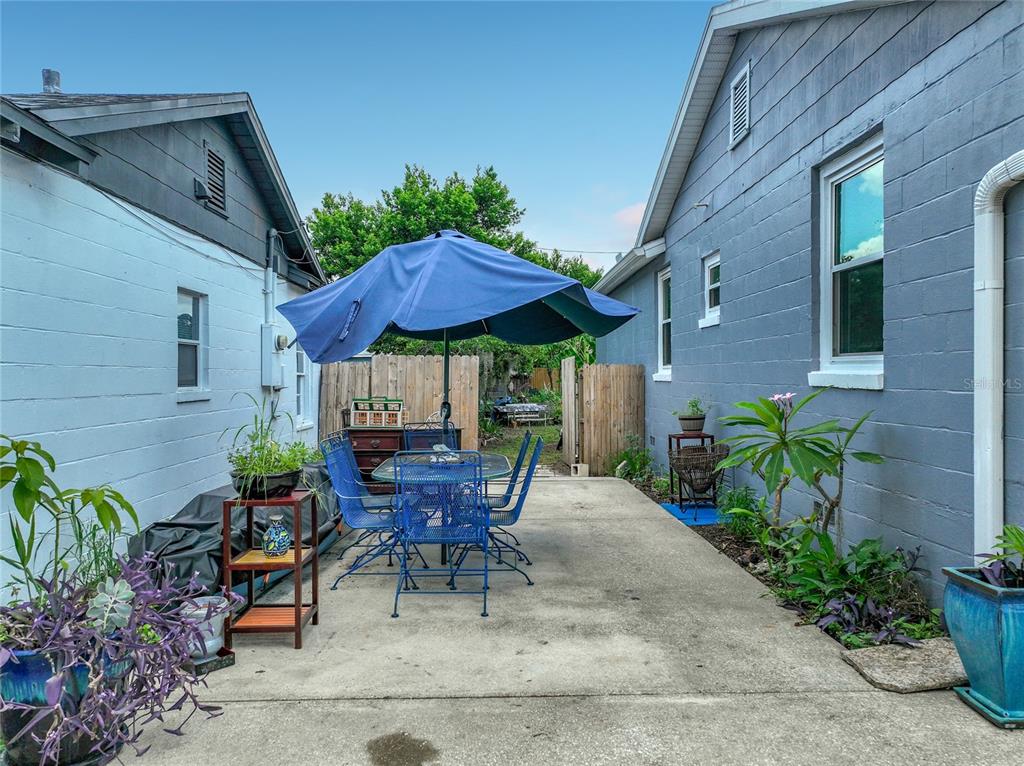 A concrete patio between two houses features a blue dining set under a patio umbrella — 2509 SHANNON ROAD, ORLANDO, FL