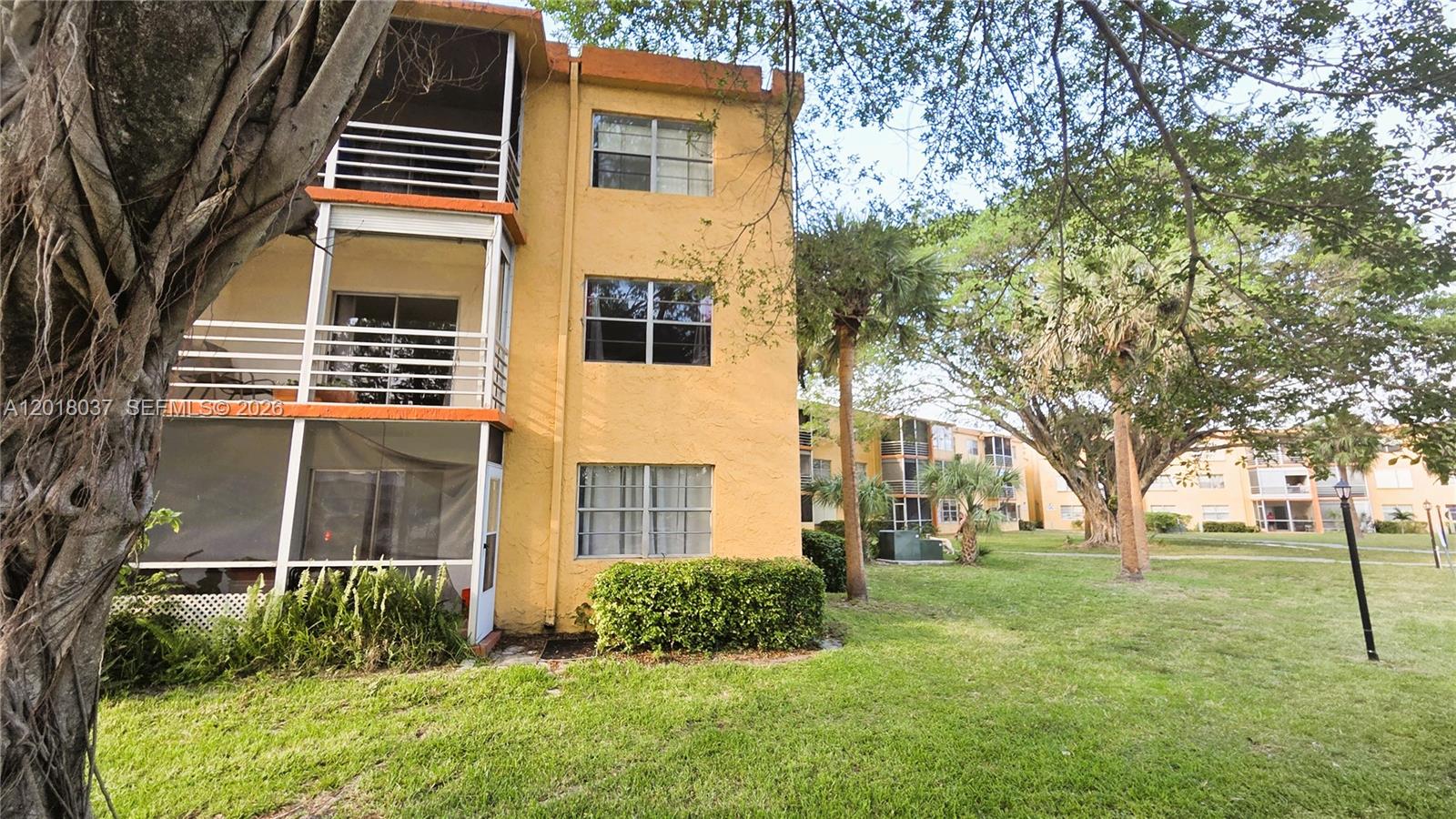 A three-story yellow apartment building features screened balconies and is surrounded by green lawns — 4344 NW 9th Ave # 2B, Deerfield Beach FL 33064, DEERFIELD BEACH, FL