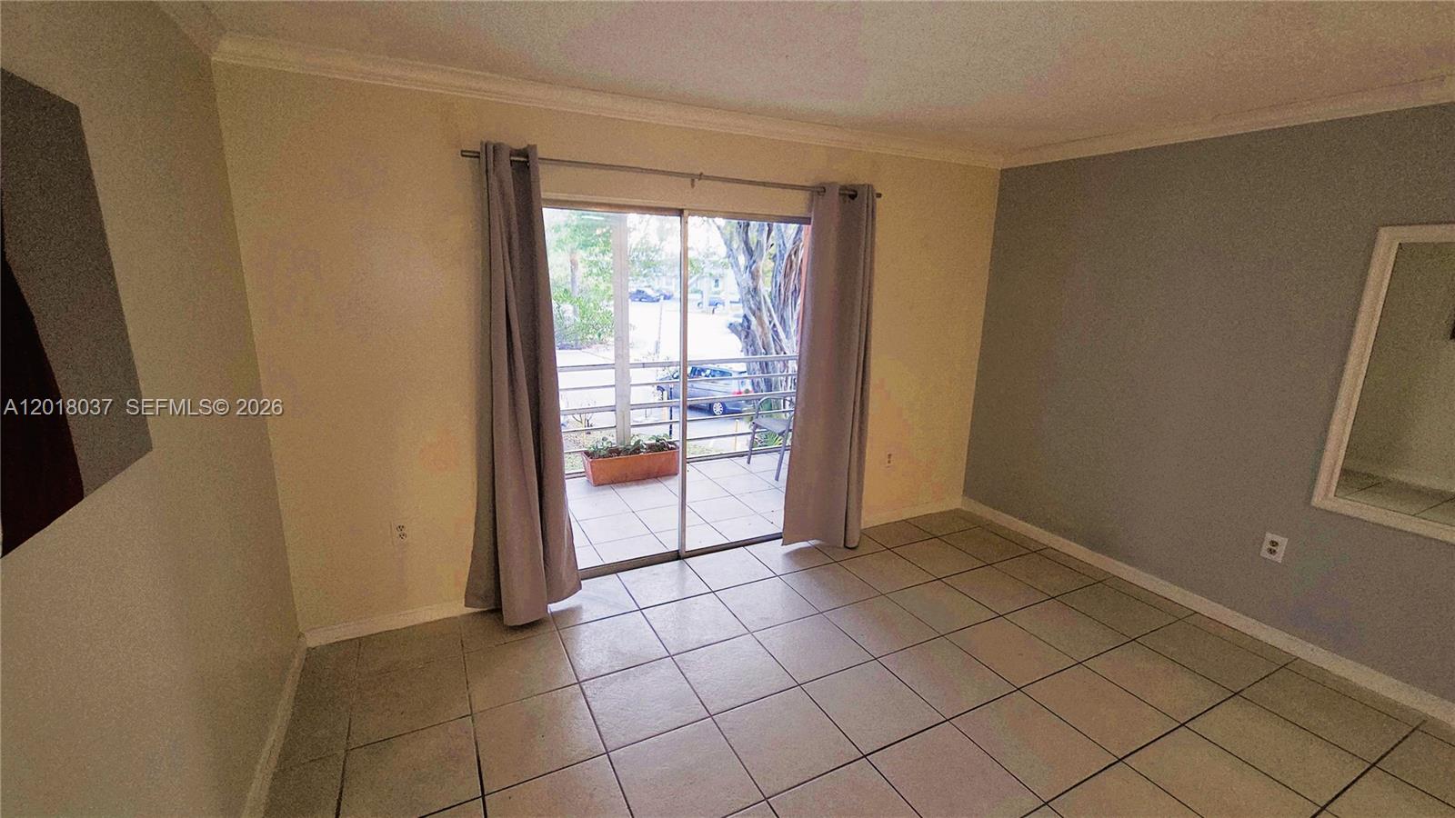 An empty room features light-colored tile flooring, gray walls, and a sliding glass balcony door — 4344 NW 9th Ave # 2B, Deerfield Beach FL 33064, DEERFIELD BEACH, FL