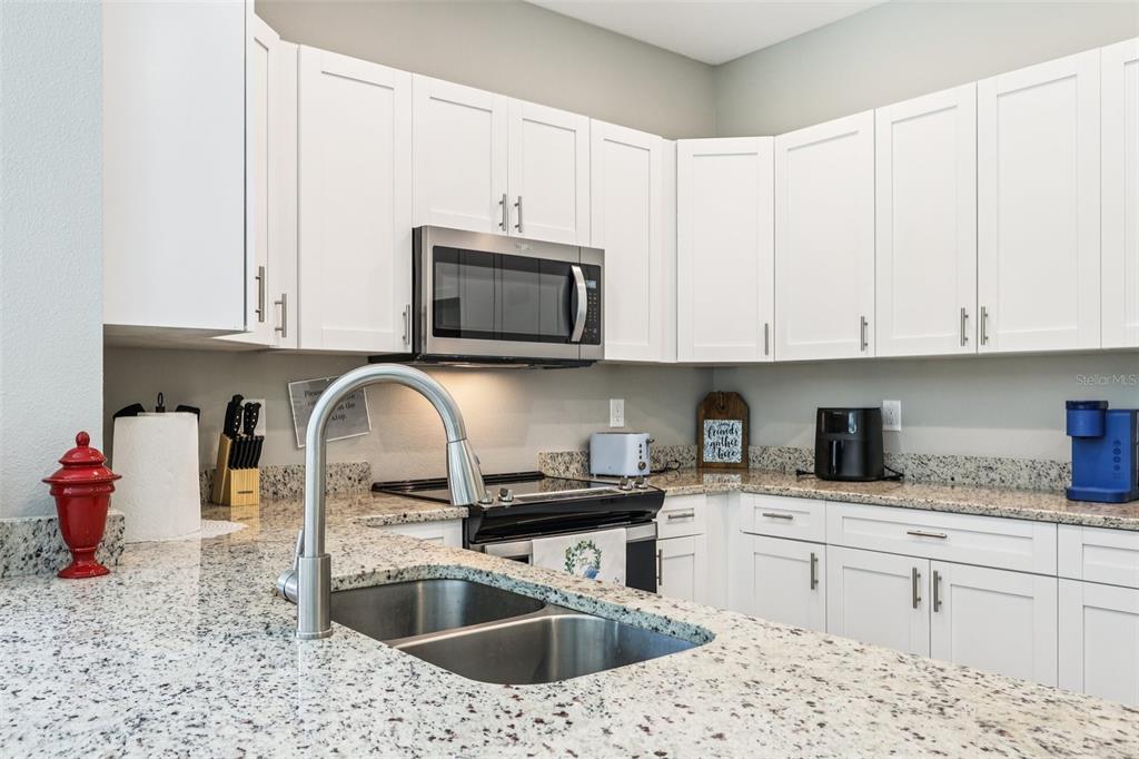A kitchen features white cabinets, granite countertops, a stainless steel microwave, and a double sink — 1108 FOX LAKE DRIVE, LAKELAND, FL