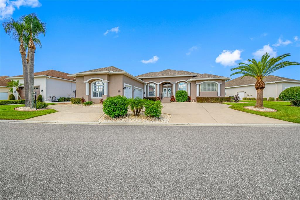 A tan single-story house with a multi-car garage and palm trees under a blue sky — 6750 HUNTINGTON HILLS BOULEVARD, LAKELAND, FL