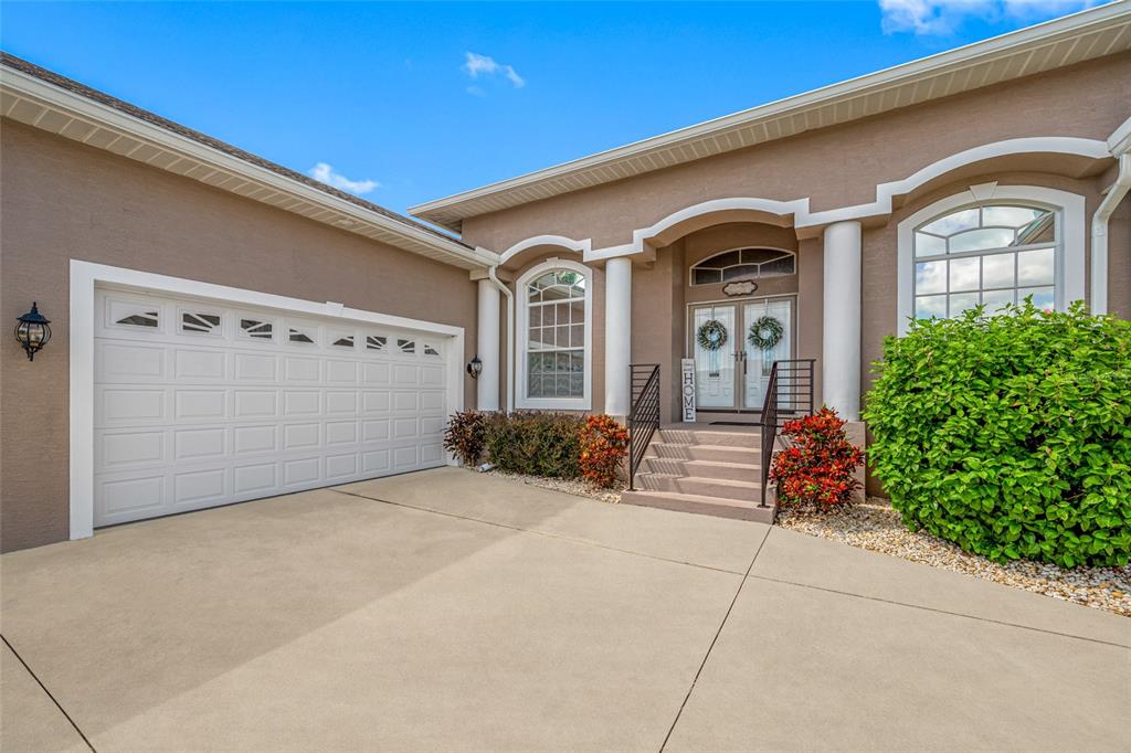 A beige house exterior features a two-car garage, a front entryway with columns, and landscaping — 6750 HUNTINGTON HILLS BOULEVARD, LAKELAND, FL