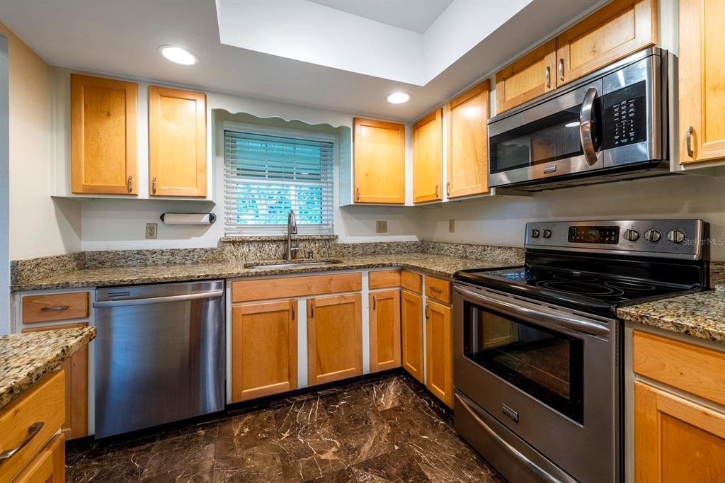 A kitchen features light wood cabinets, granite countertops, stainless steel appliances, and dark marble flooring — 110 N TREMAIN STREET UNIT 202, MOUNT DORA, FL