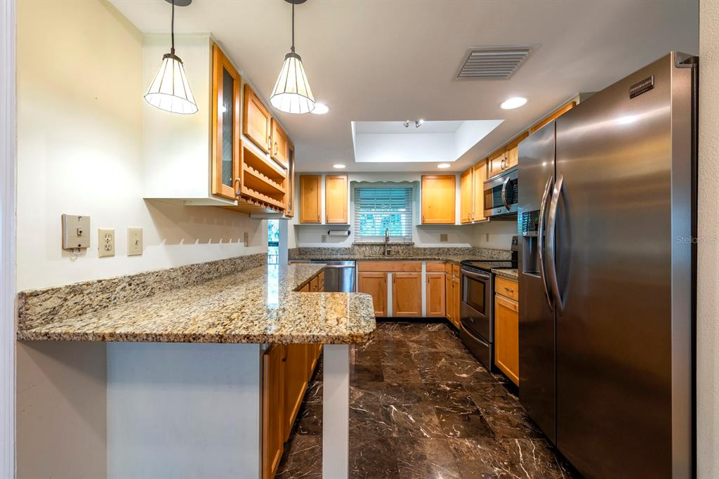 A kitchen features wood cabinets, granite countertops, stainless steel appliances, and dark marble flooring — 110 N TREMAIN STREET UNIT 202, MOUNT DORA, FL