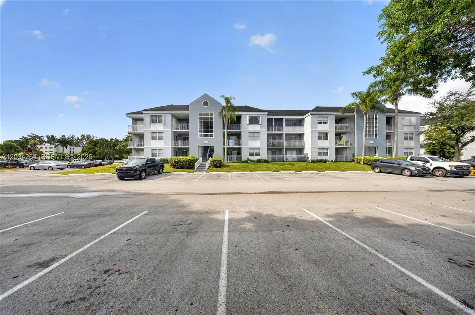 A three-story apartment building with a gray facade stands behind a large paved parking lot — 8540 SW 212th St # 202, Cutler Bay FL 33189, CUTLER BAY, FL