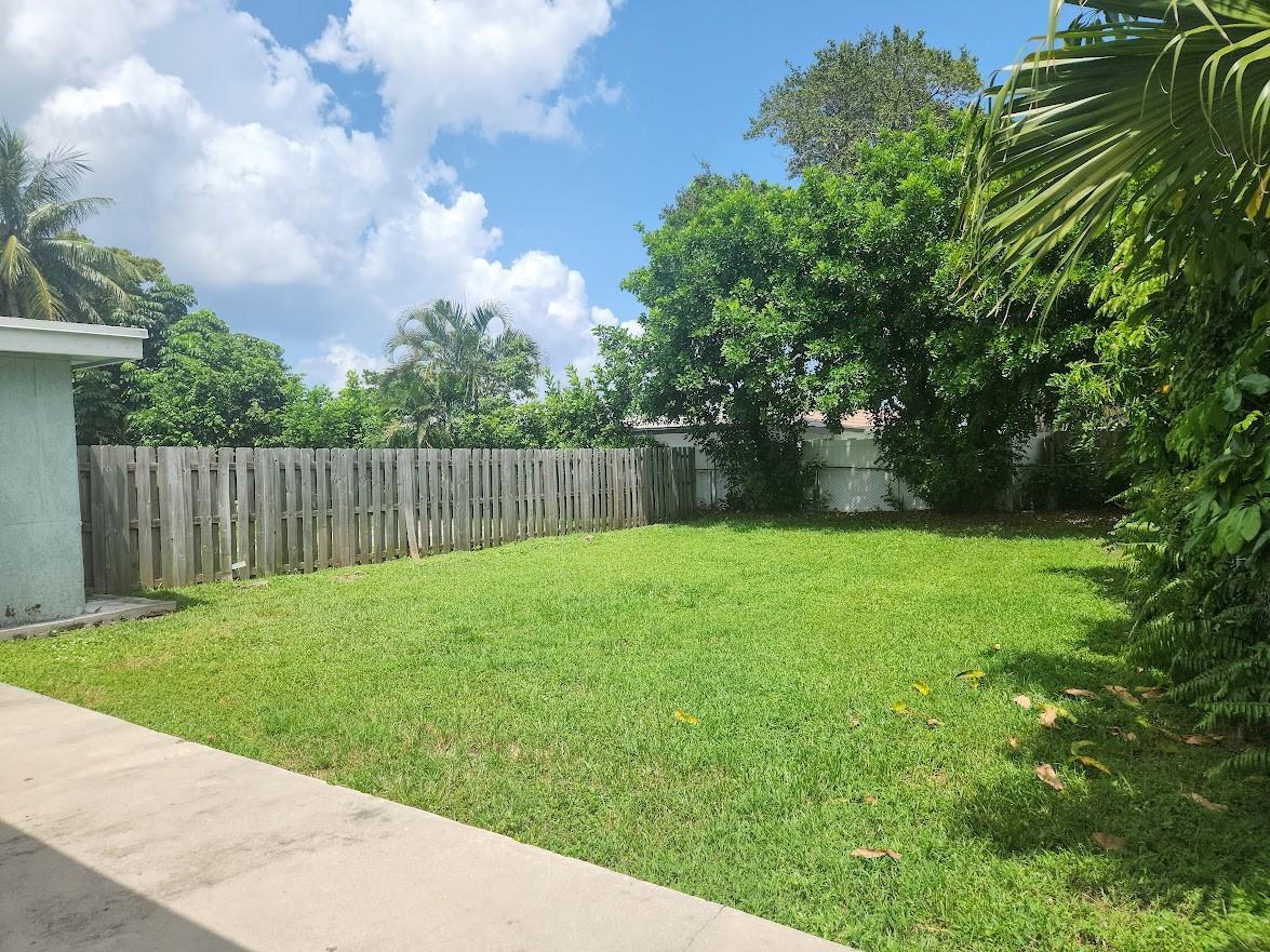 A grassy backyard features a wooden fence, mature trees, and a concrete patio area — 2940 NE 19th Terrace Side, Lighthouse Point FL 33064, LIGHTHOUSE POINT, FL