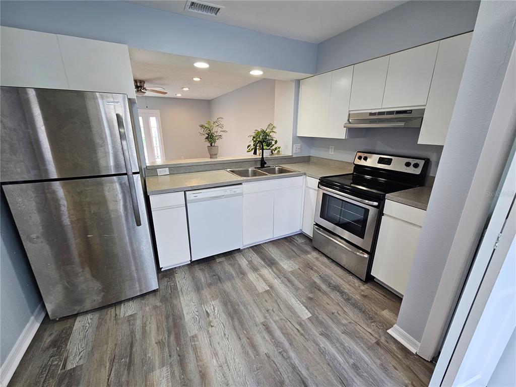 A kitchen features stainless steel appliances, white cabinets, gray countertops, and wood-look flooring — 13817 STONE MILL WAY, TAMPA, FL